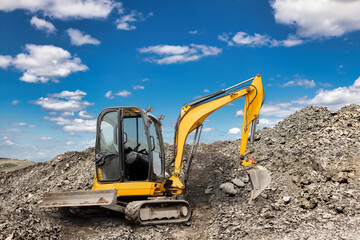 Obraz premium A yellow excavator is digging into a mound of dirt at a construction site. The sun shines brightly, casting shadows on the rugged terrain
