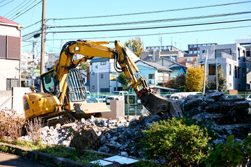 Urban demolition site with a yellow excavator working to tear down a residential building in a...