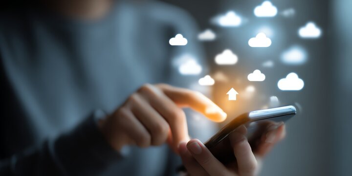 A close-up of a person's hand using a smartphone, with cloud icons representing technology and digital connectivity floating above. Illustrates modern communication and innovation.