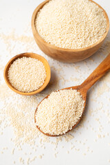 White sesame seeds in wooden spoon and bowl on white background. Organic sesame, cooking ingredient, Asian seasoning, source of calcium. Space for text. Top view flat lay