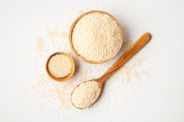 White sesame seeds in wooden spoon and bowl on white background. Organic sesame, cooking ingredient, Asian seasoning, source of calcium. Space for text. Top view flat lay