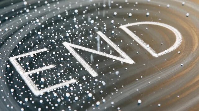 Close-up of the word 'END' written in white on a dark, textured surface surrounded by fine particles, creating a striking visual