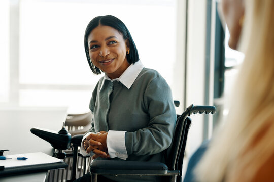 Young professional woman in a wheelchair talking to a colleague at work