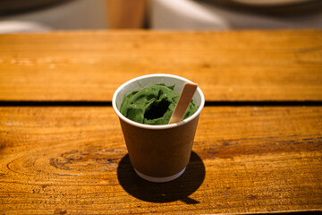 Green dessert in paper cup on wooden table with spoon