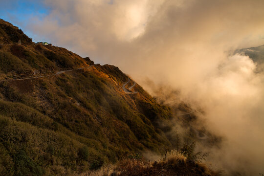 Dramatic sunset view of the winding Silk Route road in Zuluk, Sikkim, amidst clouds.