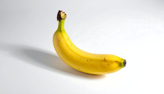 Solitary banana lies on a stark white surface, casting a shadow, showing yellow color with some browning spots
