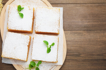 Tasty lemon bars with powdered sugar and mint on wooden table, flat lay. Space for text