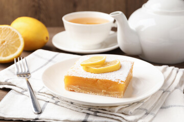 Tasty lemon bar with powdered sugar served on wooden table, closeup