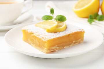 Tasty lemon bar with powdered sugar and mint on white wooden table, closeup