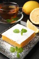 Tasty lemon bar with mint, fresh fruits and tea on black table, closeup
