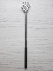 A metal back scratcher in the form of a hand on a rod. Vertical.