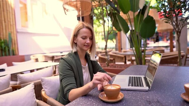 Smiling blonde woman stirring cappuccino at a coffee shop