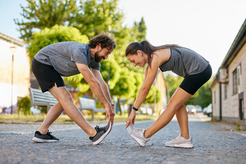 Two individuals engage in a stretching routine in a community park, enjoying the outdoors and focusing on their fitness. The sun is shining, creating a lively atmosphere.