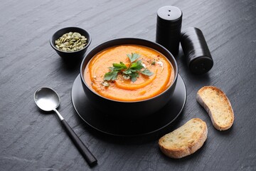 Tasty pumpkin cream soup with parsley in bowl served on grey table