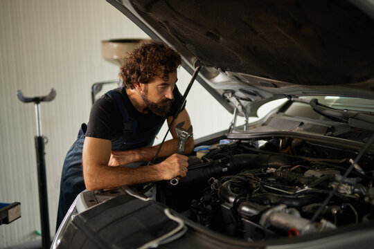 A skilled car mechanic inspects the engine of a vehicle, using tools to perform repairs. The workshop is well-lit and organized, creating a productive environment for work.
