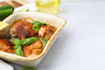 Tasty cooked chicken thighs with basil in baking dish and ingredients on light grey table, closeup. Space for text