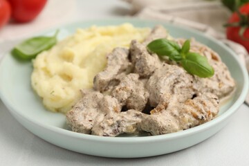 Delicious beef stroganoff with mashed potatoes and basil on white table, closeup