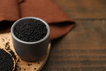 Aromatic black caraway in bowl and spoon on wooden table, closeup. Space for text
