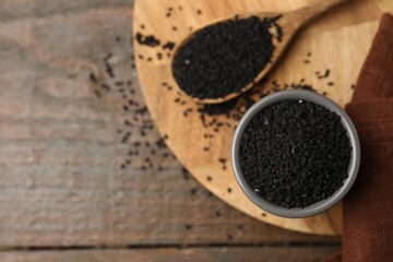 Aromatic black caraway in bowl and spoon on wooden table, top view. Space for text