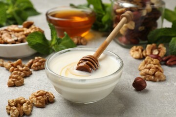 Delicious Greek yogurt with honey, nuts and mint on light grey table, closeup