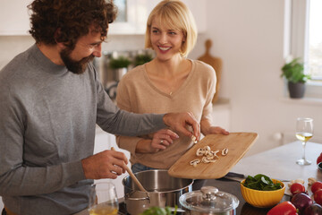 A man and woman share a joyful moment in a sunny kitchen, chopping mushrooms and preparing a delicious meal with fresh vegetables and herbs.