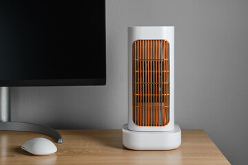 Electric heater placed on a wooden desk beside a computer monitor in a cozy indoor setting