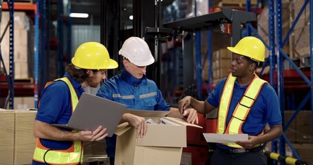 warehouse supervisor and two workers including african american staff coordinating cargo handling task in slowmotion while checking box and laptop near pallet in logistic distribution facility - Powered by Adobe