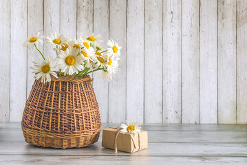 Bouquet of white daisies flowers in wicker basket and craft gift box on a wooden table and wooden background with copy space