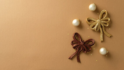 Top view of gold and bronze festive bows with pearl ornaments on a minimalist tan background.