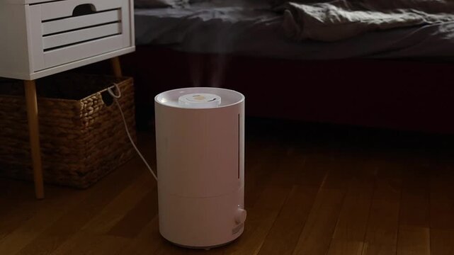 A modern white ultrasonic cool mist humidifier releasing visible vapor in a dimly lit bedroom. Used to improve air quality, health, and comfort, creating a soothing home atmosphere.