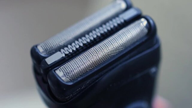 Extreme macro close-up of a modern electric shaver head, highlighting the perforated metal foil mesh texture and central cutting element for men's grooming and hygiene.