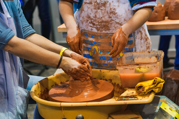Hands coated in clay while shaping a ceramic piece on a pottery wheel in a craft workshop