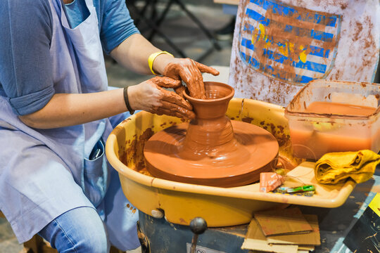 Hands forming a clay vessel on a pottery wheel as part of a hands-on ceramic workshop.