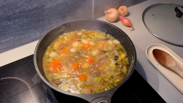 Traditional French pot-au-feu or vegetable stew simmering in a pan on a modern cooktop.