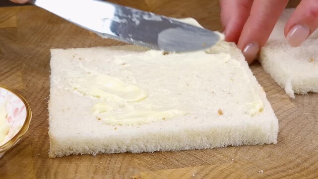 Hand spreading soft butter on a slice of white bread with a metal knife