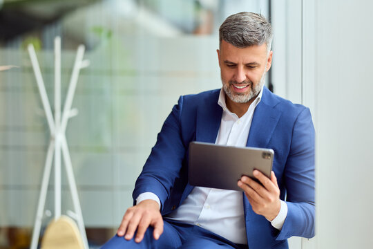 Professional Man in Blue Suit Using Tablet in Modern Office Lounge for Business