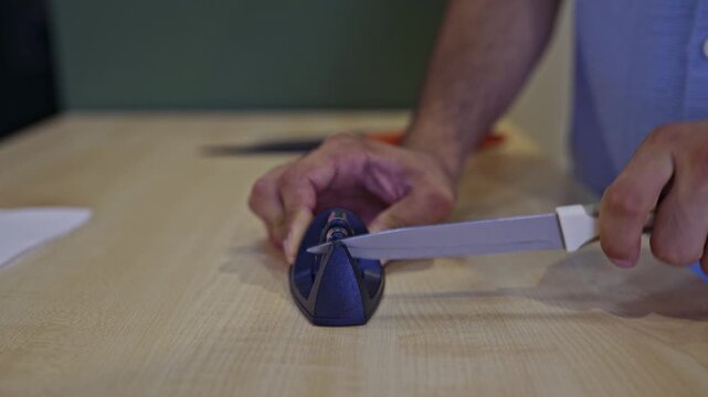 A detailed close-up shot of hands using a knife sharpener to hone a kitchen knife's blade, capturing the process with authentic sounds. Ideal for cooking, culinary, or kitchen-related projects.