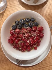 Morning breakfast kasha porridge with berries served in a ceramic bowl on wooden table with spoon, fresh fruits, cozy atmosphere, healthy nutritious meal, morning sunlight, delicious homemade traditio