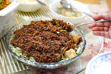 Close-up of Rojak Tauhu, a traditional Malaysian tofu salad with fresh vegetables and savory dark sauce in a glass bowl on a striped surface.