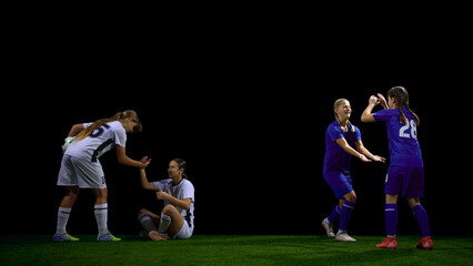 Fototapeta premium Female soccer players helping teammate after fall during match. Concept of fair play lessons, sports ethics materials, social values education, teamwork campaigns.