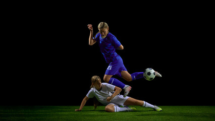 Fototapeta premium Teenage female soccer players in sliding tackle duel during active play. Concept of youth defensive training, contact-technique instruction, tactical coaching, match analysis.