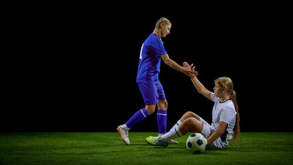 Teenage female soccer player offering hand to help opponent stand up. Concept of youth sport values, respect education, fair-play messaging, character-building materials.