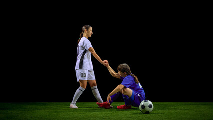 Teenage girls soccer player helping teammate rise after fall during match. Concept of youth teamwork programs, leadership lessons, support-culture promotion, educational materials.