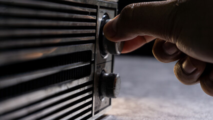 A hand adjusting the tuning knob of a weathered radio, with dramatic shadows highlighting texture and vintage craftsmanship. Suitable for themes of retro sound and manual controls.