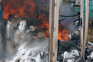 A close-up of an intense fire: open, bright red flames and plumes of thick black smoke rise from the burning materials. The photo conveys the chaos and heat of the fire.