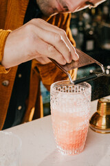 A man is making a drink with a shaker. The drink is pink and is in a glass