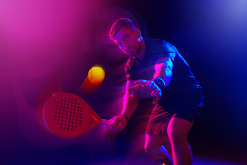 Man playing padel tennis under colorful lights in a dimly lit environment