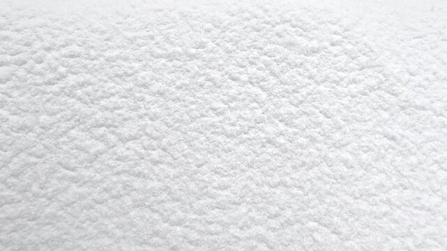 Still view of smooth snow surface with minor texture variations as light snowfall continues, showing subtle movement of tiny flakes across bright winter ground in soft daylight