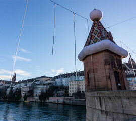 A decorative turret on a bridge over the Rhine River in Basel, adorned with a large Santa hat for the Christmas season, with the cityscape in the background
