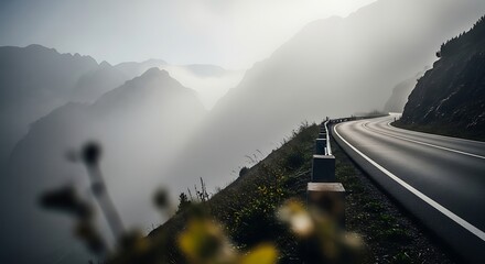 An empty, winding road snakes through a majestic, fog-covered mountain range at dawn.